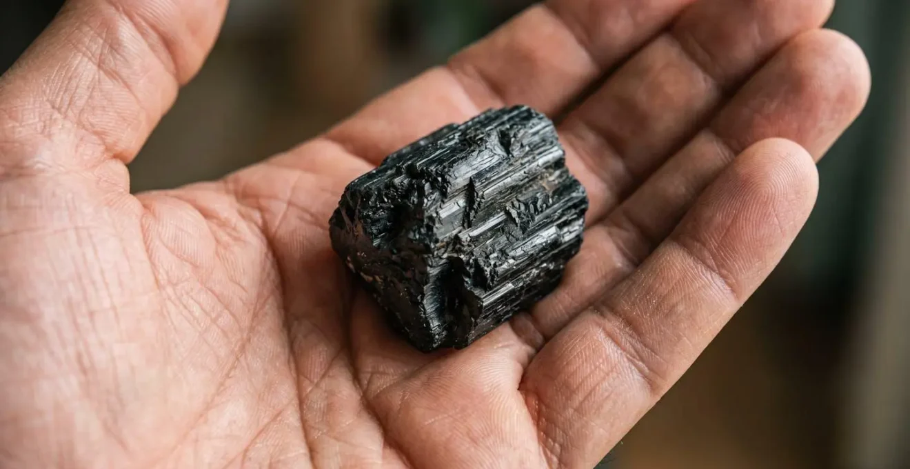 Gros plan macro d'une pierre naturelle noire aux reflets subtils tenue dans une paume de main avec une profondeur de champ très réduite