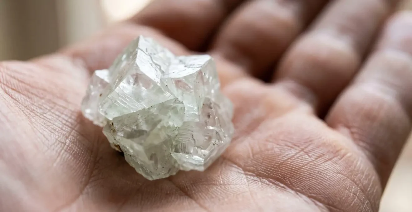 Pierre d'apophyllite tenue dans une paume de main en gros plan, textures cristallines visibles, lumiere naturelle douce