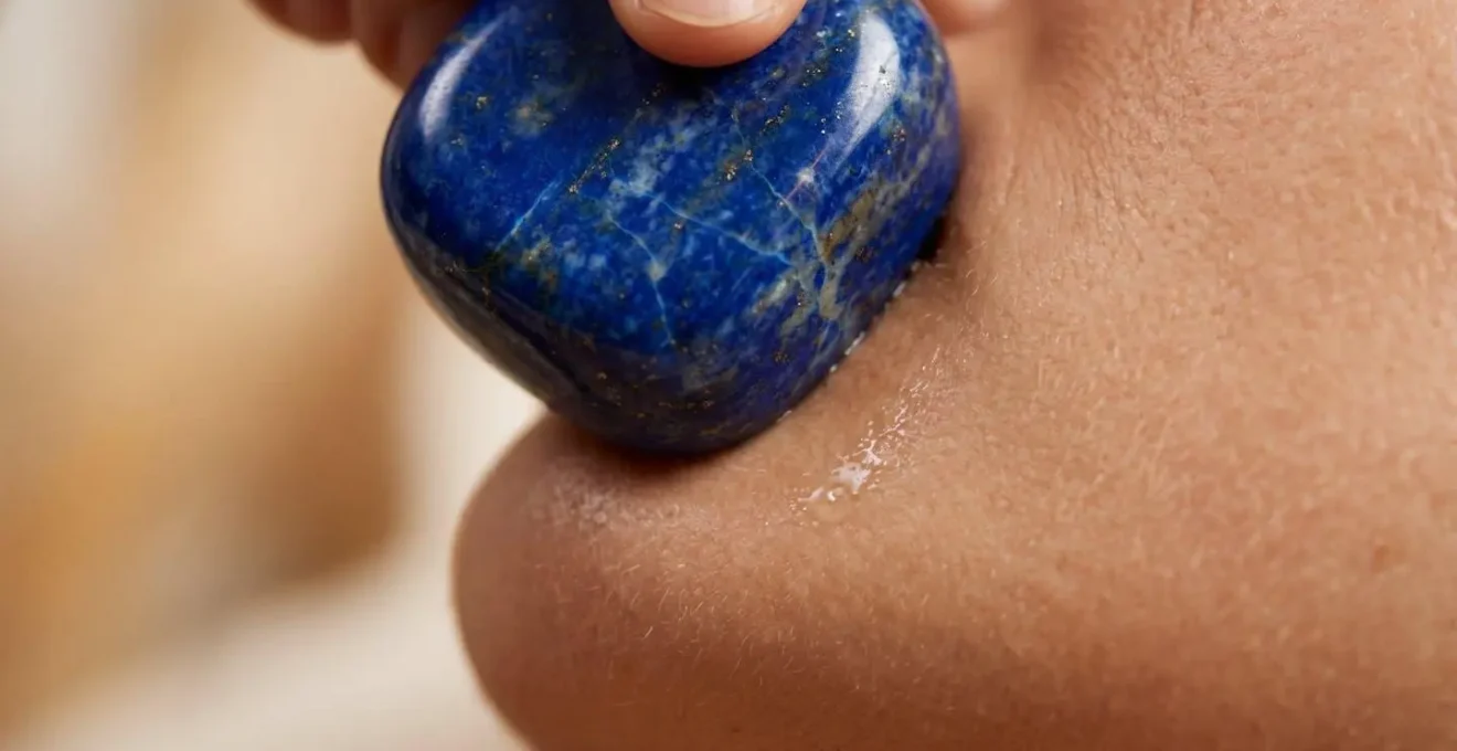 Gros plan macro sur une pierre de lapis-lazuli pressée délicatement sur la ligne de la mâchoire pour libérer les tensions émotionnelles