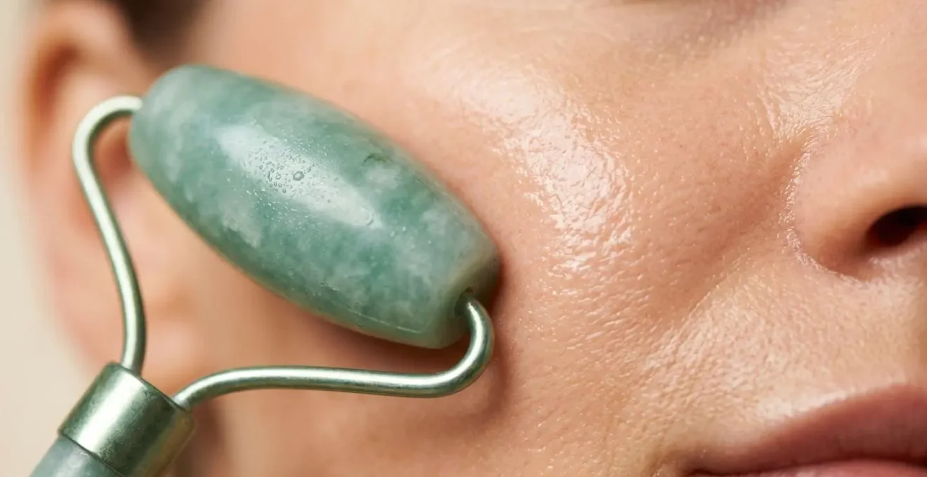 Gros plan sur une main effectuant un massage facial avec un rouleau de jade sur une peau apaisée
